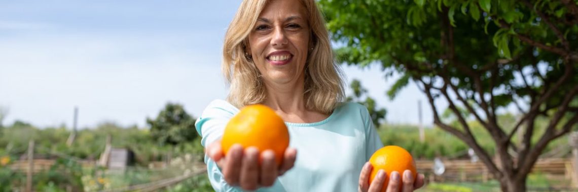 Cheerful woman in garden holding fresh organic oranges, enjoying nature.